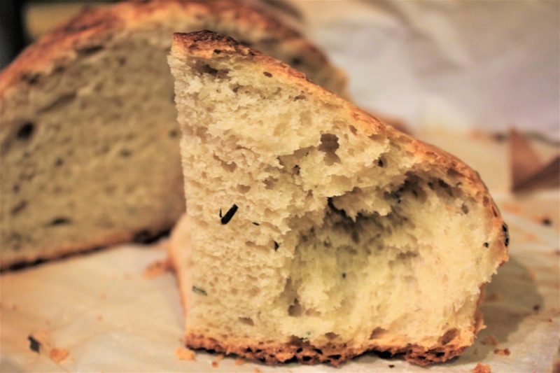 Closeup of chunk of no-knead Mediterranean bread with loaf in the background