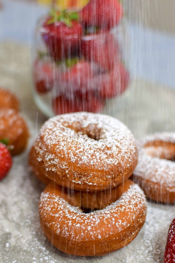 closeup of powdered sugar falling on 3 strawberry cake donuts