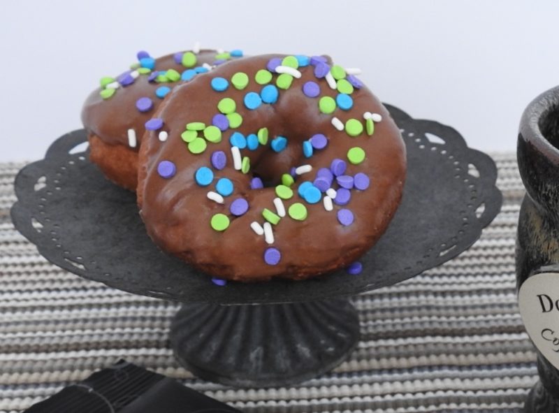 two chocolate-frosted donuts with colorful sprinkles on a cake stand