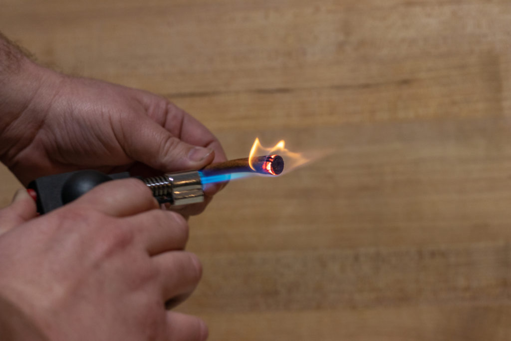 Hands using a kitchen blowtorch to scorch a cinnamon stick