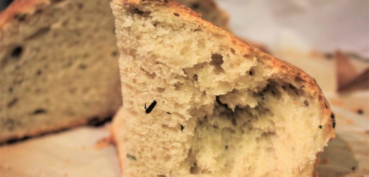 Closeup of chunk of no-knead Mediterranean bread with loaf in the background